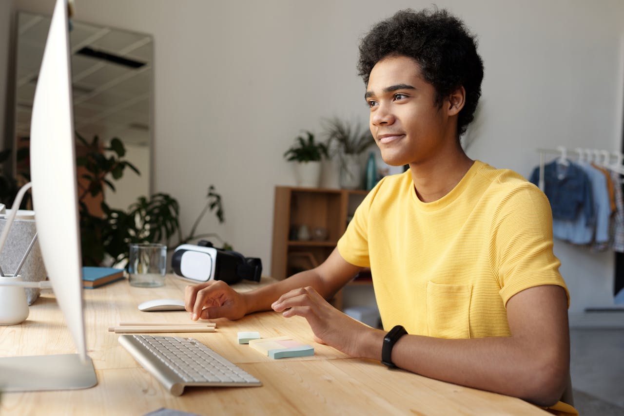 services-04 Teenager smiling while studying online at home. Modern education setup with computer and VR headset.